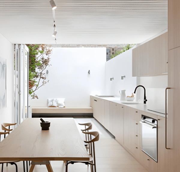 Projeto de cozinha minimalista em madeira clara com design escandinavo. Móveis planejados, bancada branca e área de jantar integrada com vista para o pátio.