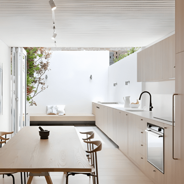 Projeto de cozinha minimalista em madeira clara com design escandinavo. Móveis planejados, bancada branca e área de jantar integrada com vista para o pátio.