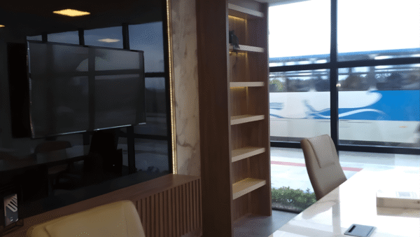 Design de sala de reunião moderna com mesa de conferência em mármore. Painel de TV preto, móveis em marcenaria com acabamento em madeira e iluminação embutida.